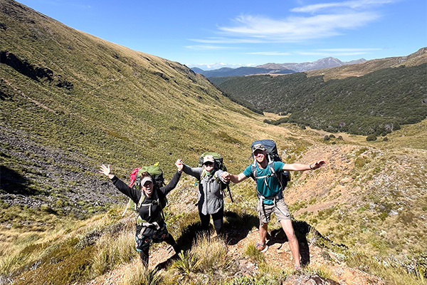 Three hikers wave their hands at the head of a mountain valley