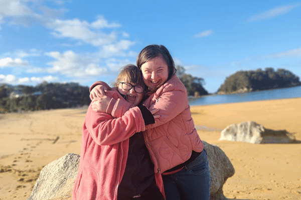 Two young women smile on the golden sand beach